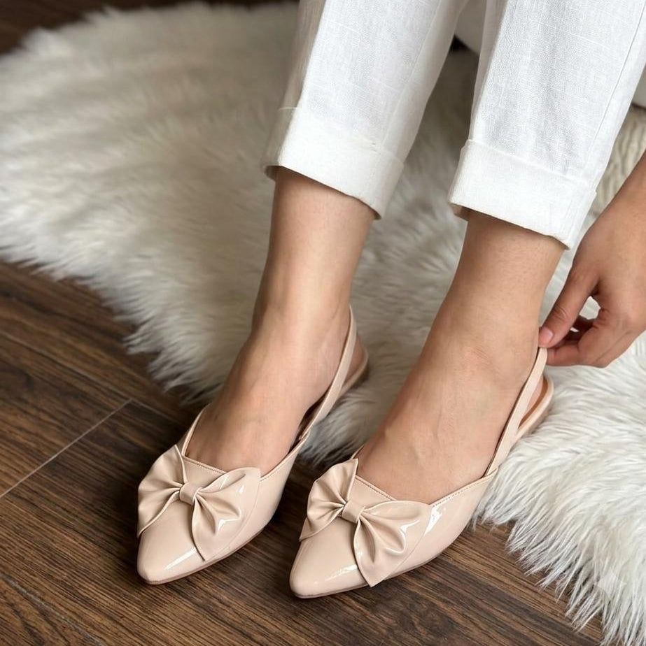 Beige flats with bow details worn by a person on a wooden floor.