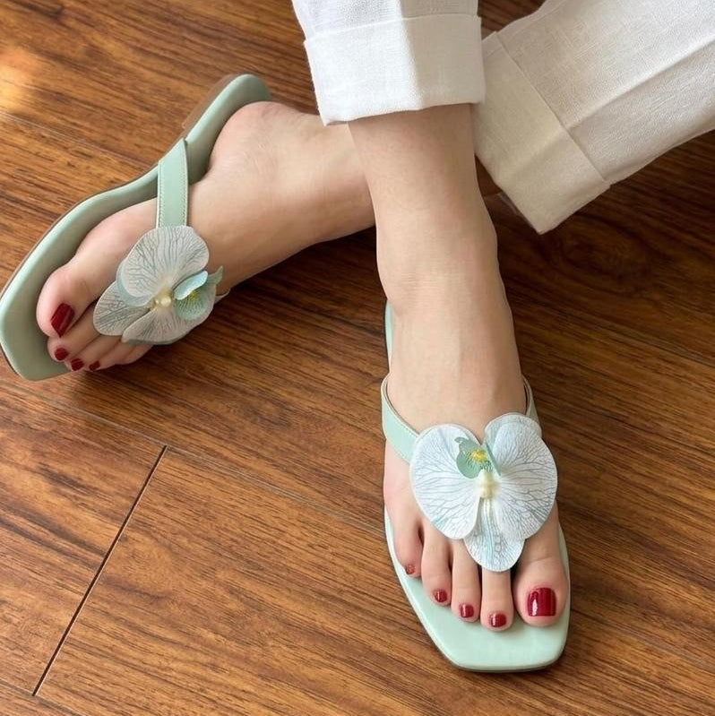 Green sandals with floral designs worn on a wooden floor