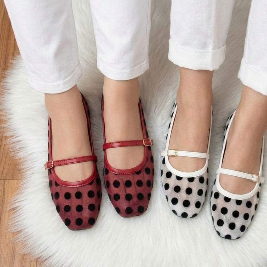 Two pairs of polka dot shoes worn with white pants on a fluffy white rug.
