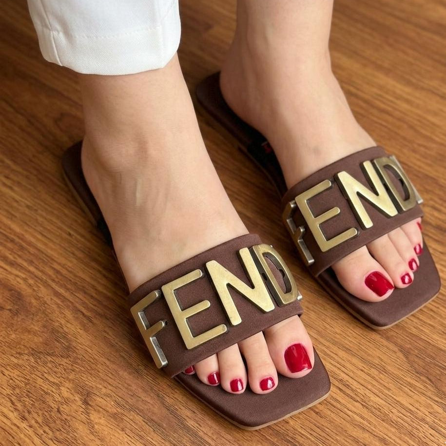 Brown slides with 'FENDI' logo worn on a wooden floor