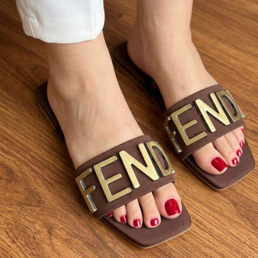 Brown slides with 'FENDI' logo worn on a wooden floor