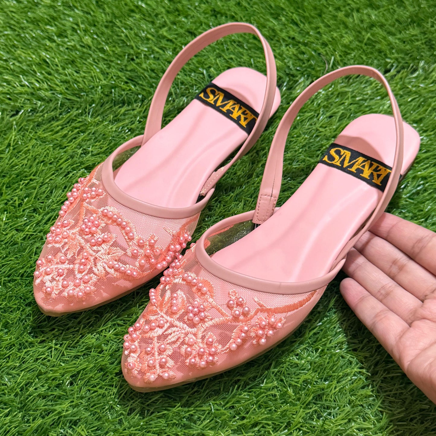 Pink embellished shoes with 'Swarovski' logo on a green grass background