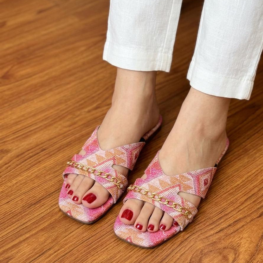 Pink sandals with gold chains worn on a wooden floor