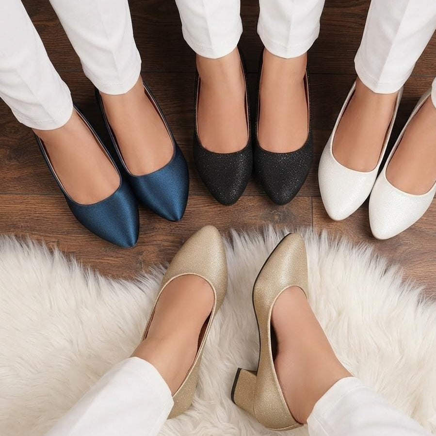 Six women's pointed-toe flats shown in different colors, worn by models in white pants on a wooden floor with a white faux-fur rug. The shoes include blue, black glitter, white, and champagne beige.