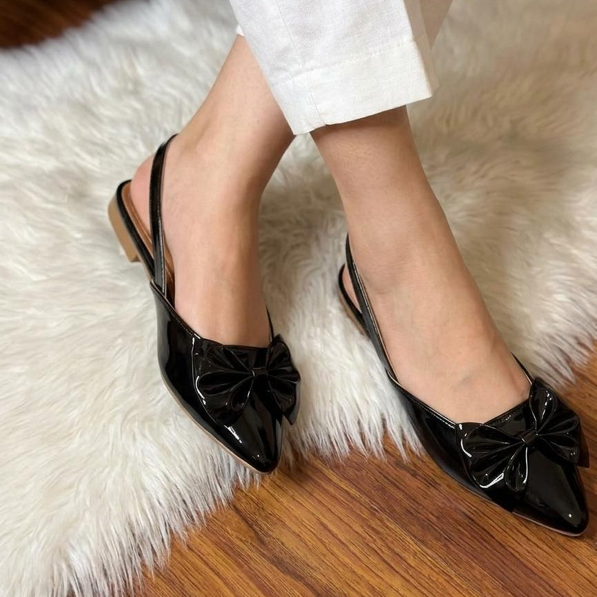 Black flat shoes with bow details worn on a white fur rug.