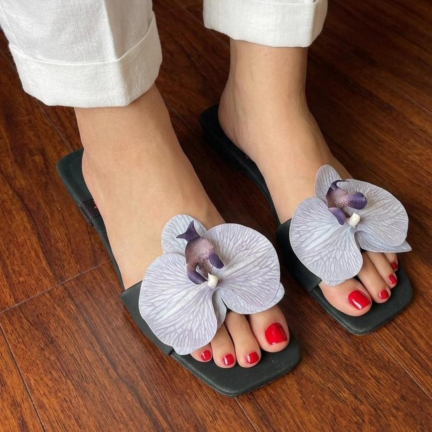 Black sandals with floral designs worn on a wooden floor