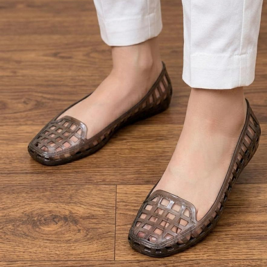 Brown flat shoes with mesh design worn by a person on a wooden floor.