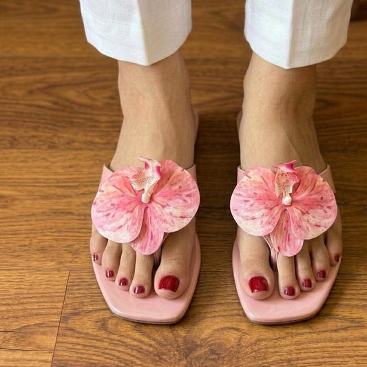 Pink sandals with floral designs worn on a wooden floor