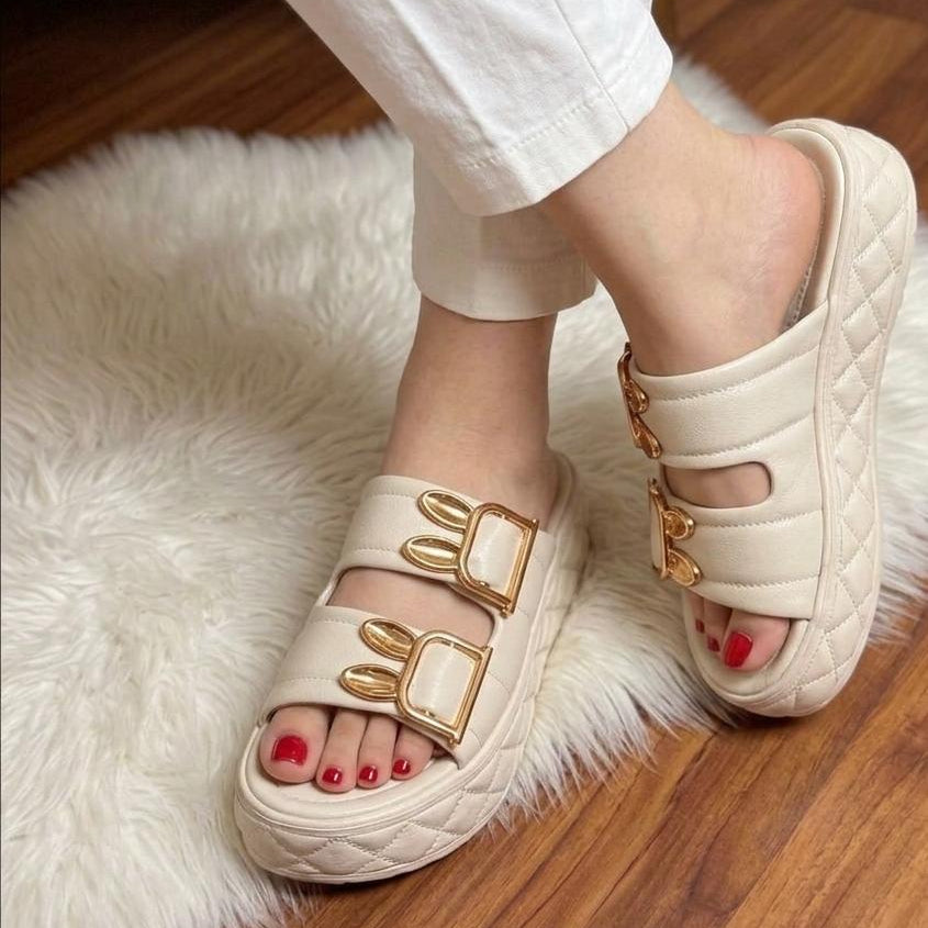 White sandals with gold accents worn indoors on a fluffy white rug.