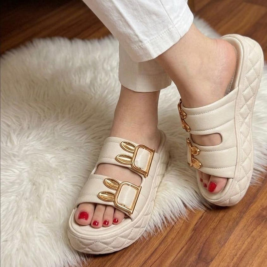 White sandals with gold accents worn indoors on a fluffy white rug.