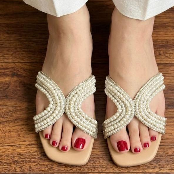 Pearl sandals worn with white pants on a wooden floor