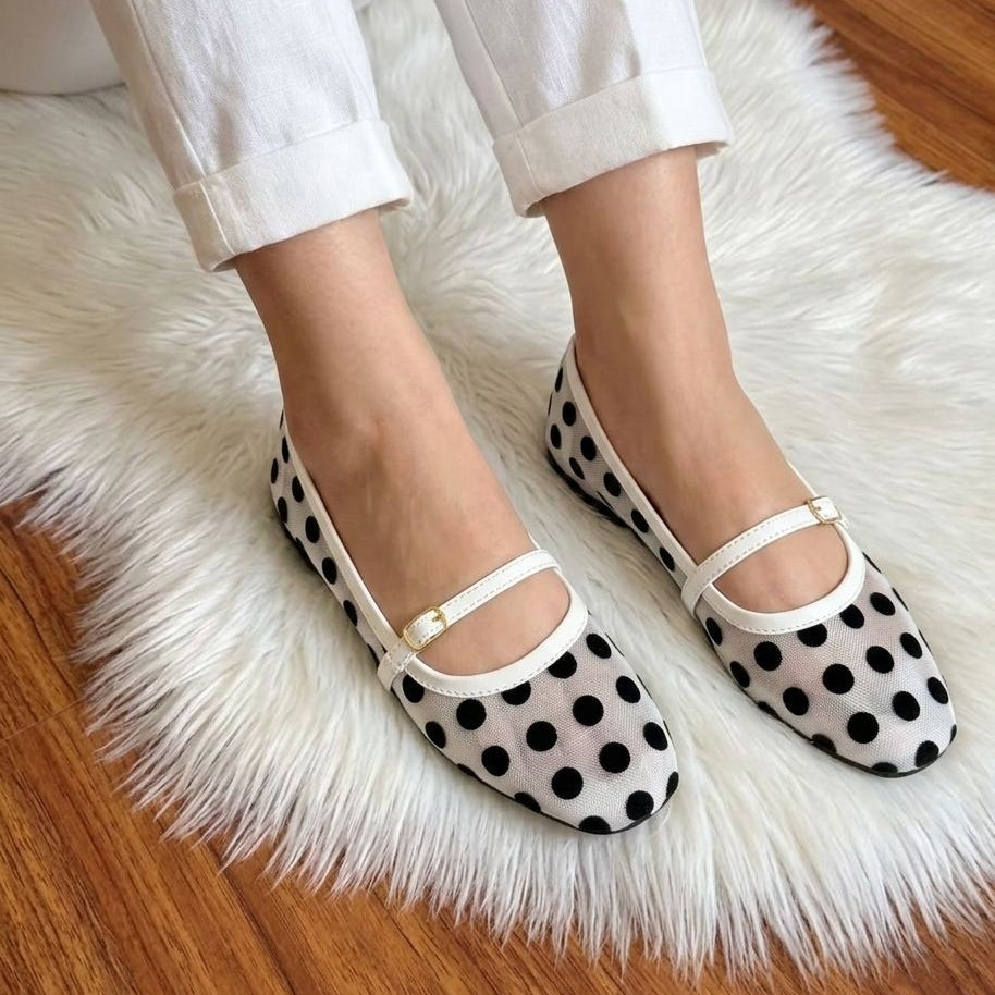 Polka dot shoes worn on a fluffy white rug with wooden floor.