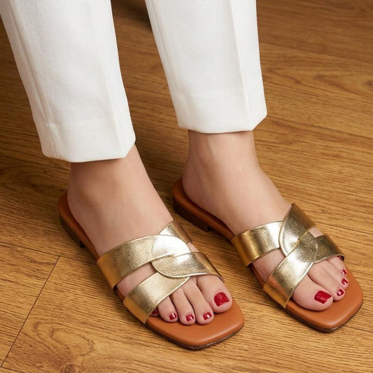 Gold sandals worn with white pants on a wooden floor