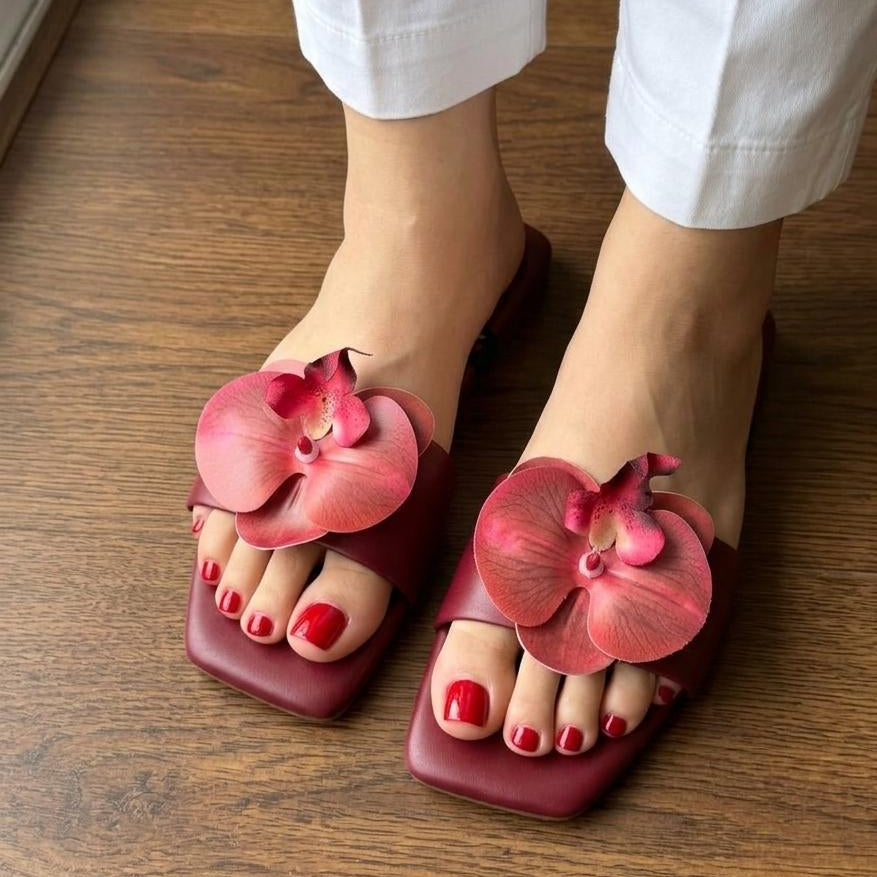 Pink sandals with floral designs worn on a wooden floor.