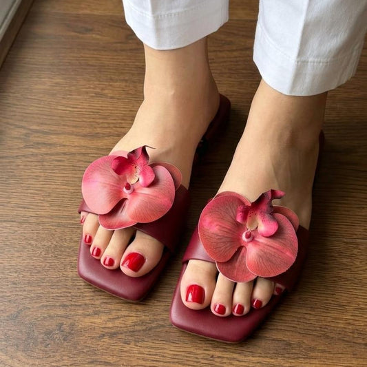 Pink sandals with floral designs worn on a wooden floor.