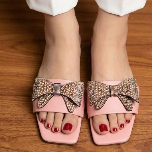 Pink sandals with decorative bows worn on a wooden floor