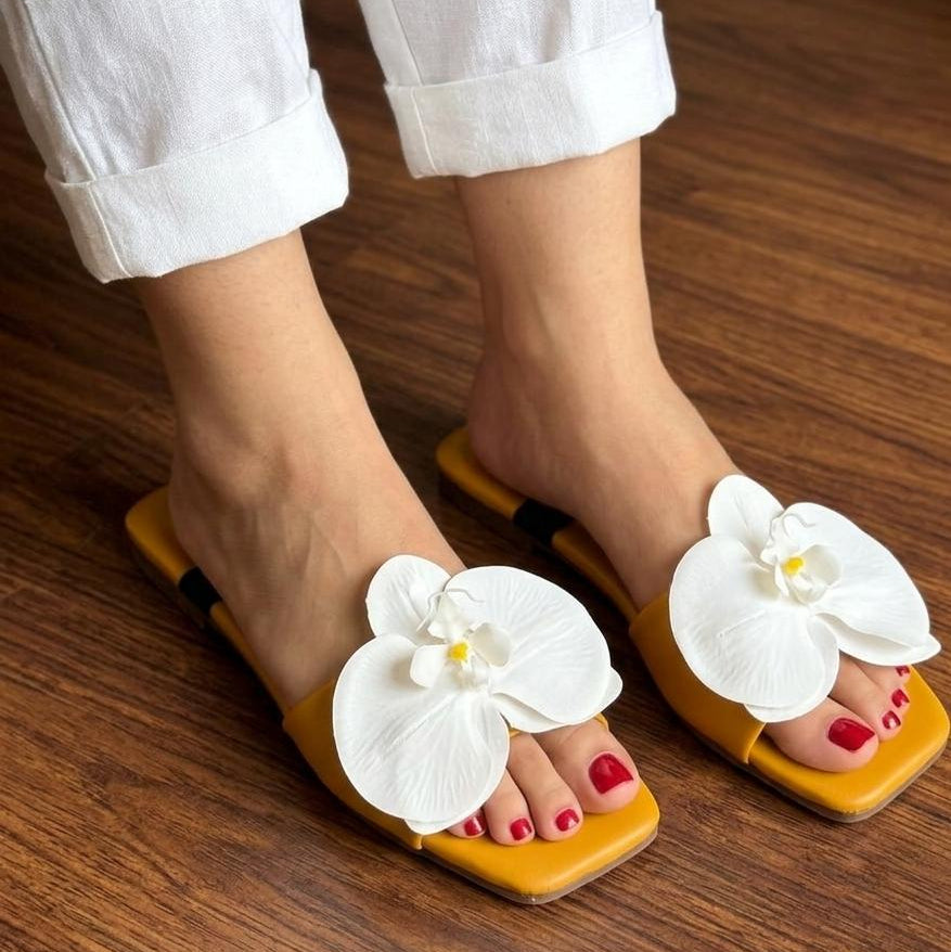 Yellow sandals with white floral decorations worn on a wooden floor.