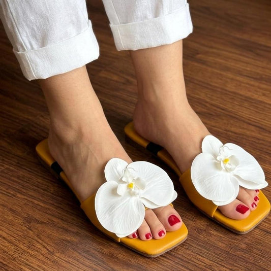 Yellow sandals with white floral decorations worn on a wooden floor.