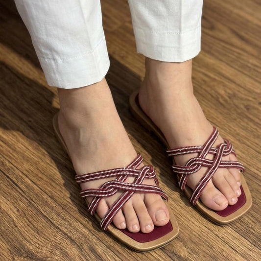 Red and white sandals worn with white pants on a wooden floor