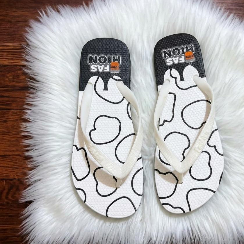 Pair of white flip-flops with black heart patterns on a fluffy white rug.