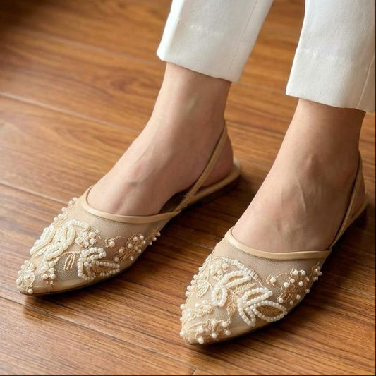 Beige flats with floral embroidery worn by a person on a wooden floor