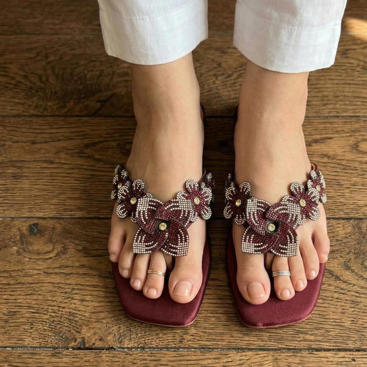 Maroon sandals with floral embellishments on a wooden floor