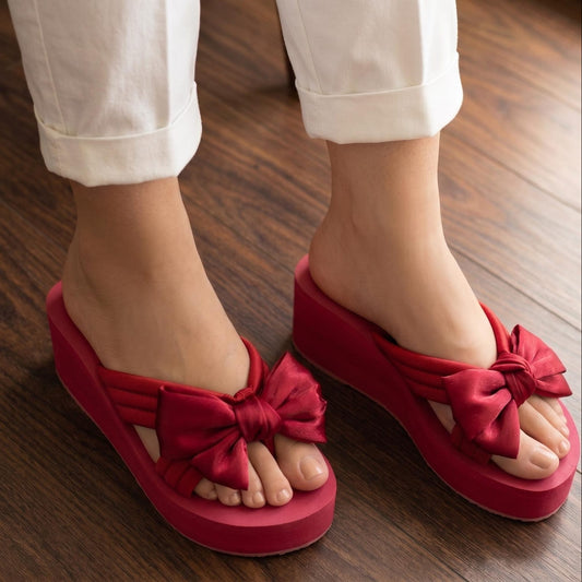 Red sandals with bow details worn on a wooden floor