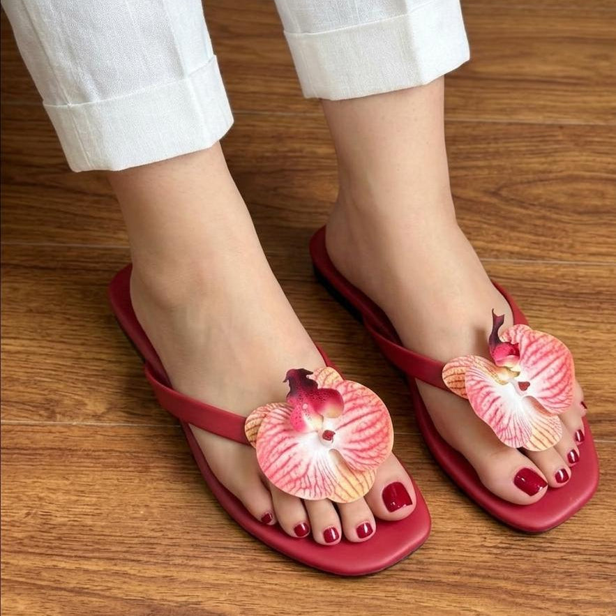 Red sandals with floral designs worn on a wooden floor