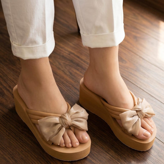 Beige sandals with bow details worn on a wooden floor