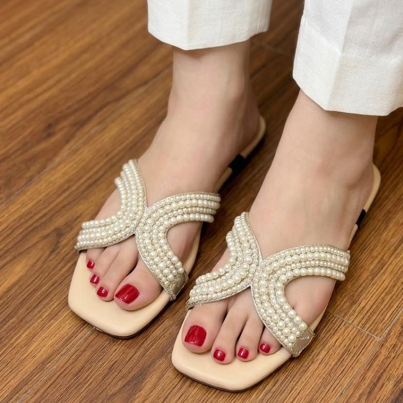 Beige sandals with pearl detailing worn on a wooden floor