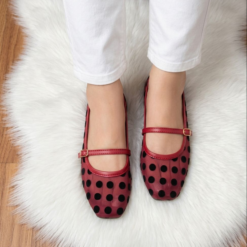 Red polka dot shoes worn with white pants on a fluffy white rug.