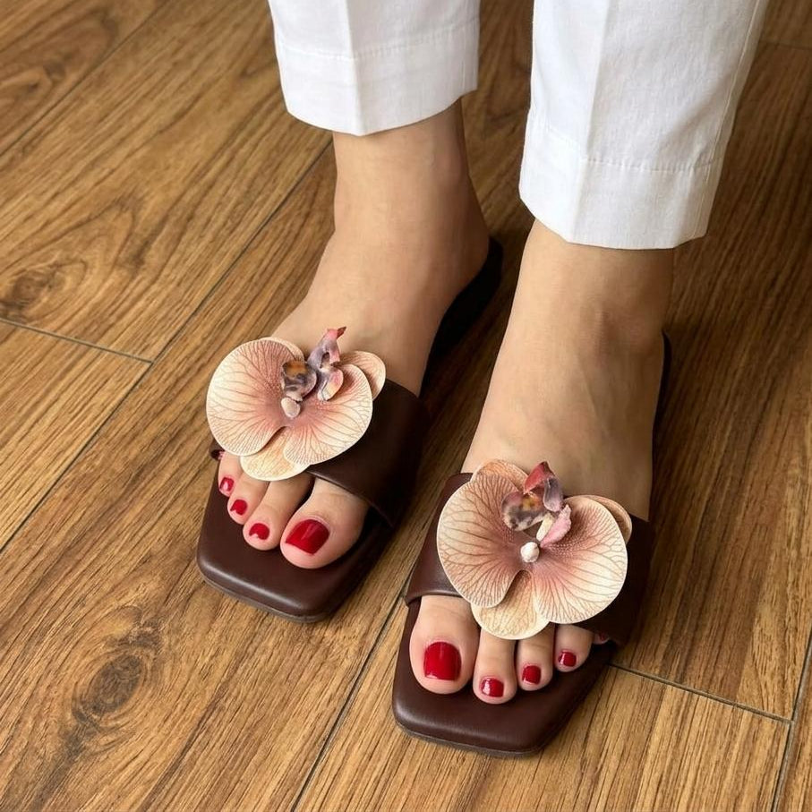 Brown sandals with floral designs worn on a wooden floor