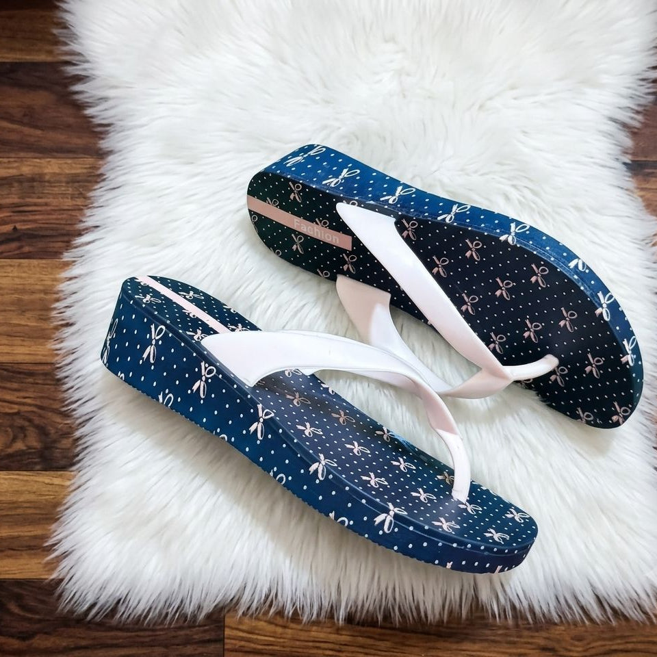 Pair of blue flip-flops with white patterns on a fluffy white rug.