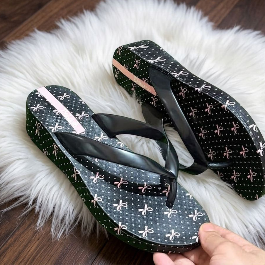 Pair of black flip-flops with white patterns on a fluffy white rug.