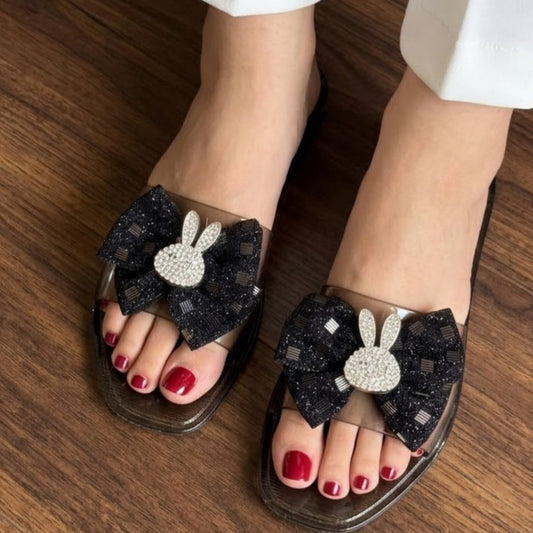 Black sandals with decorative elements worn on a wooden floor