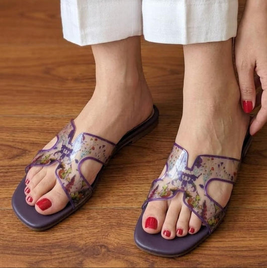 Transparent sandals with floral patterns worn on a wooden floor