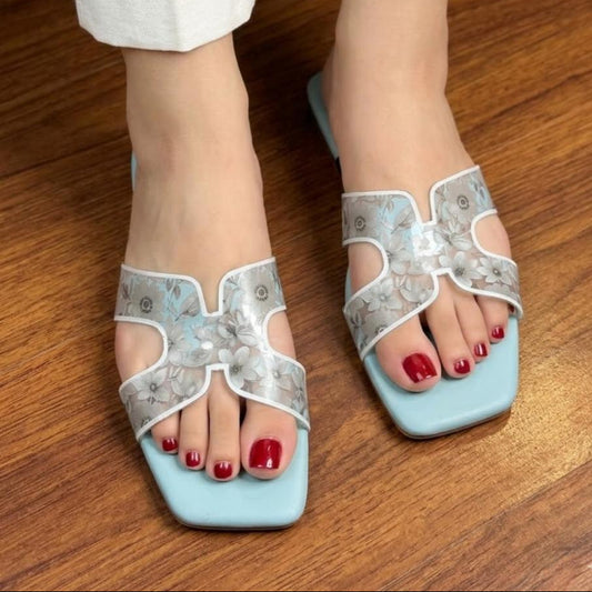 Light blue sandals with decorative straps worn on a wooden floor.