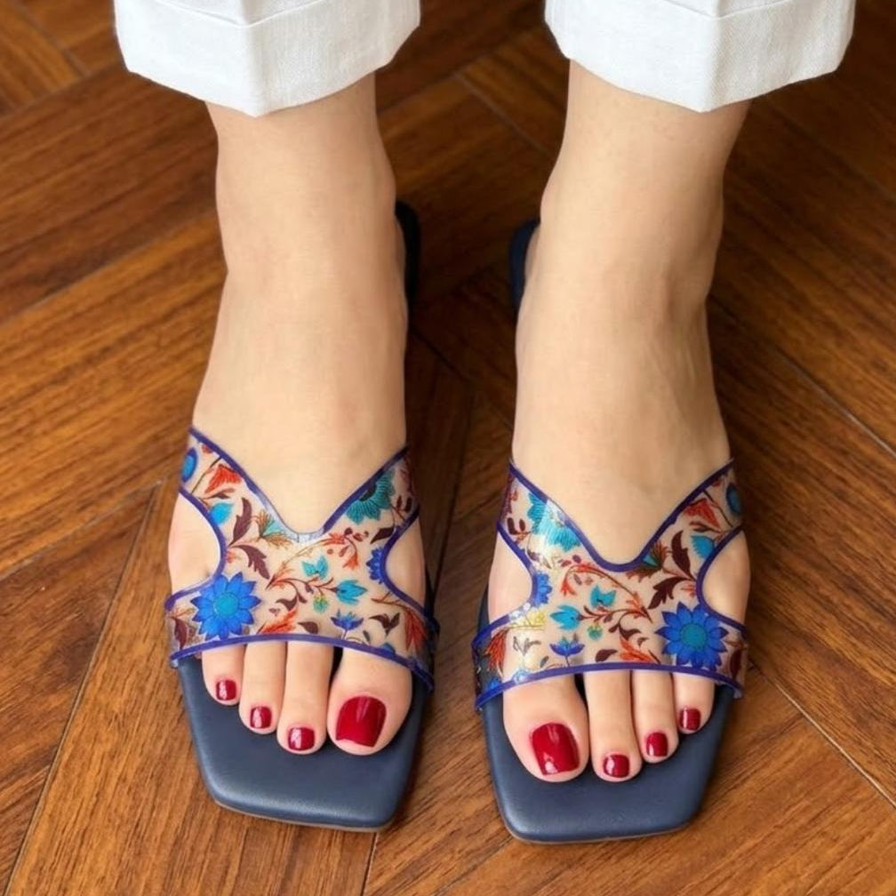 Colorful sandals with floral patterns worn on a wooden floor.