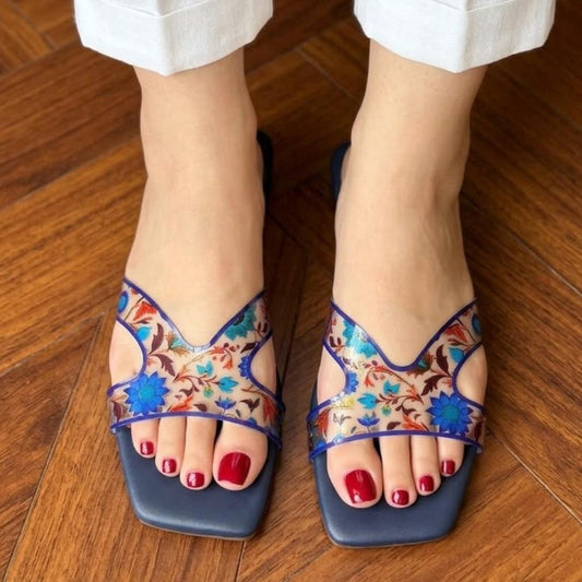 Colorful sandals with floral patterns worn on a wooden floor.