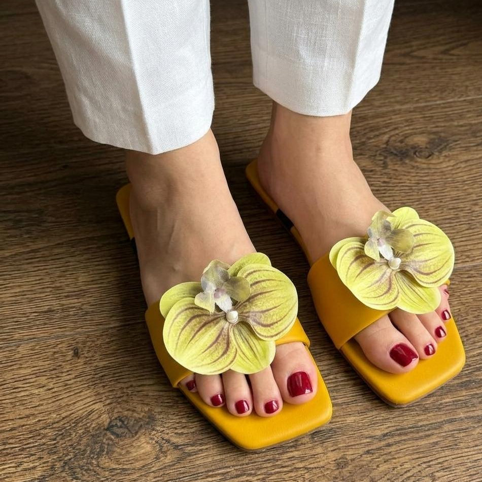 Yellow sandals with floral decorations worn on a wooden floor