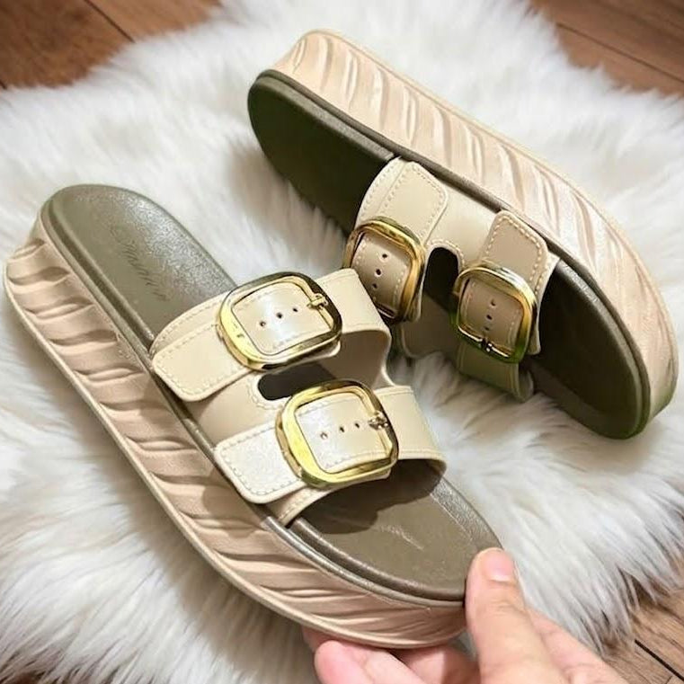 Pair of beige sandals with gold buckles on a white fur surface.