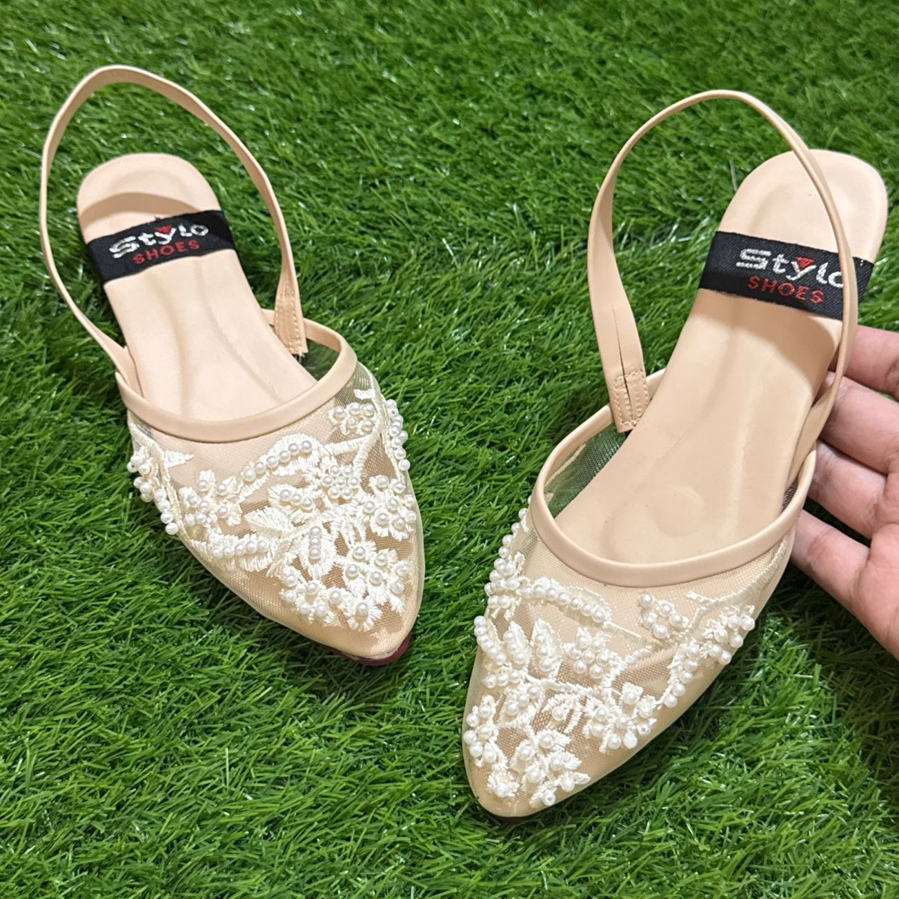 Beige flat shoes with white lace details on a green grass background