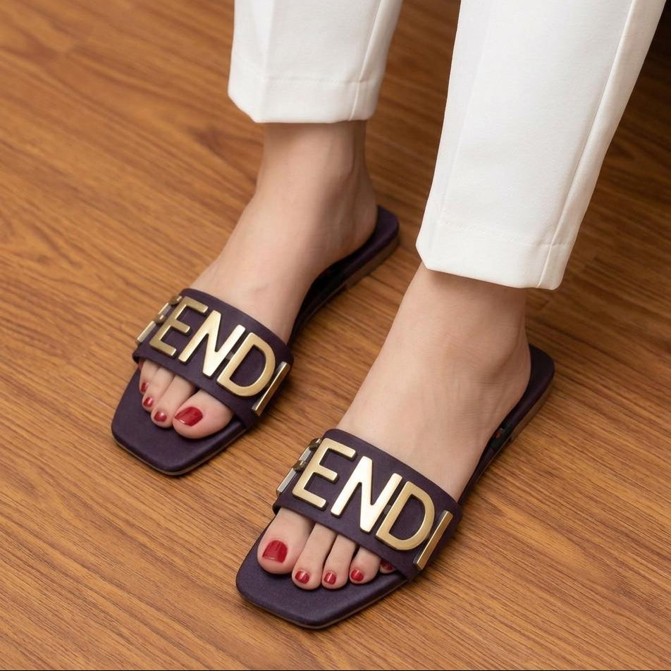 Black slides with gold 'Fendi' logo worn on a wooden floor