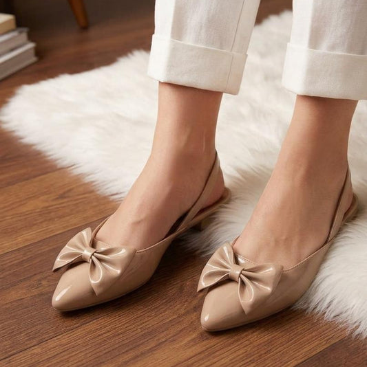 Beige flat shoes with bow details worn by a person on a wooden floor.