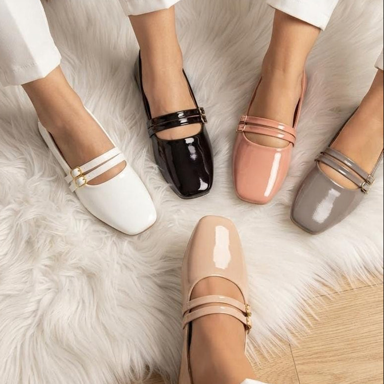 Four women's Mary Jane flat shoes in white, black, blush pink, and taupe, shown on feet wearing white pants on a white faux fur rug.